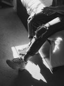 Person wearing ripped jeans and white sneakers sitting on a couch.
