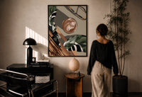 Iced Coffee Flat Lay print in a black frame on a sunlit plaster wall, a woman looking on beside a mushroom lamp