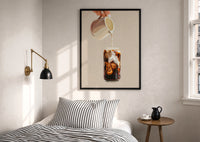Iced Latte Cream Pour print in a black frame above a bed with striped linens, a brass wall lamp and a sunlit window