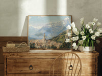 Alpine town with church tower print in an oak frame on a farmhouse dresser beside white tulips