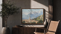 Alpine town with church tower print in a wood frame above a fluted sideboard beside an olive tree