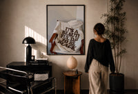 It's a Beautiful Day to Be Black print in a black frame on a sunlit plaster wall, a woman looking on beside a mushroom lamp