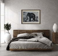 Large elephant with tusks print in a dark wood frame above a rattan bed on a plaster wall