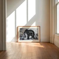 Large elephant with tusks print in an oak frame on a sunlit wood floor beneath tall window light