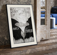 Baby cherub sitting on flower print in a black frame leaning beside a vintage door on parquet