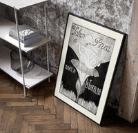 Baby cherub sitting on flower poster in a black frame leaning beside a shelf in a raw-plaster loft