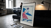 Woman holding soap box print in a slim black frame leaning on a dark sofa in a concrete print studio