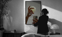 Jeweled Hands with Phone and Glass print in a slim black frame being hung on a sunlit wall in a monochrome room