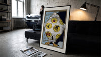 Vintage Halloween clown holding sheet print in a slim black frame leaning on a dark sofa in a concrete print studio