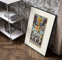 Angel blowing trumpet over rising figures poster in a black frame leaning beside a shelf in a raw-plaster loft