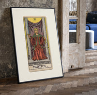 Justice tarot card figure print in a black frame leaning beside a vintage door on parquet