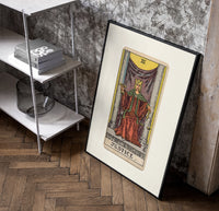 Justice tarot card figure poster in a black frame leaning beside a shelf in a raw-plaster loft