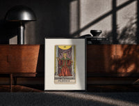 Black-framed Justice tarot card figure print on a moody console with designer coffee-table books
