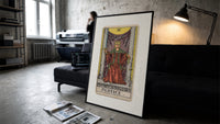 Justice tarot card figure print in a slim black frame leaning on a dark sofa in a concrete print studio