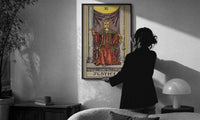 Justice print in a slim black frame being hung on a sunlit wall in a monochrome room