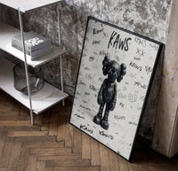 Black and white KAWS graffiti framed poster poster in a black frame leaning beside a shelf in a raw-plaster loft