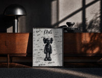 Black-framed Black and white KAWS graffiti framed poster print on a moody console with designer coffee-table books