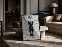 Black and white KAWS graffiti framed poster print in a black frame leaning on a travertine table in a sunlit lounge