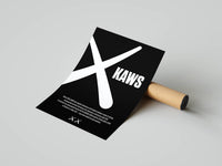 Bold KAWS typography print with XX logo on a black background unrolled across a cardboard shipping tube
