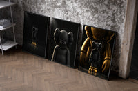 KAWS Companion Matte Black and Gold Set of 3 as black-framed prints leaning against a raw-plaster wall
