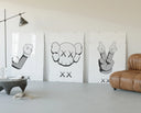 KAWS cartoon hands and skull face three-panel set displayed beside a brown leather sofa