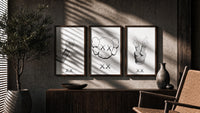 KAWS cartoon hands and skull face triptych in three walnut frames above a sideboard in a warm room