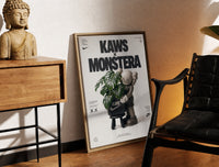Brass-framed KAWS Companion figure holding monstera plant print leaning in a warm styled corner by a sculpture