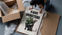 KAWS Companion figure holding monstera plant framed print being unpacked from protective bubble wrap and a box