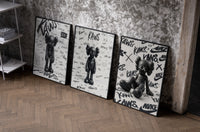 KAWS Companion figure set of three black-framed prints leaning against a raw-plaster wall