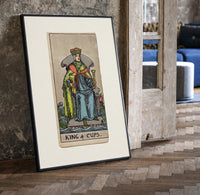 King of Cups tarot figure print in a black frame leaning beside a vintage door on parquet