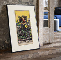 King of Pentacles tarot figure print in a black frame leaning beside a vintage door on parquet