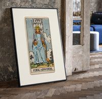 King of Swords tarot figure print in a black frame leaning beside a vintage door on parquet
