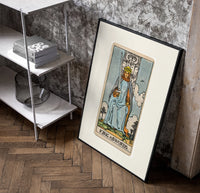 King of Swords tarot figure poster in a black frame leaning beside a shelf in a raw-plaster loft