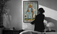 King of Swords print in a slim black frame being hung on a sunlit wall in a monochrome room