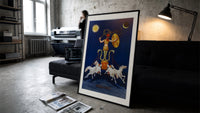 Rooster-headed Abraxas deity on chariot print in a slim black frame leaning on a dark sofa in a concrete print studio