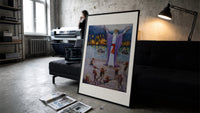 Robed magician invoking spirits print in a slim black frame leaning on a dark sofa in a concrete print studio