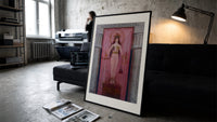 Egyptian goddess Isis unveiled print in a slim black frame leaning on a dark sofa in a concrete print studio