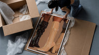 Knee-High Boots in Black and Beige framed print being unpacked from protective bubble wrap and a box
