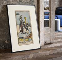Knight riding horse holding cup print in a black frame leaning beside a vintage door on parquet