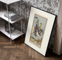 Knight riding horse holding cup poster in a black frame leaning beside a shelf in a raw-plaster loft