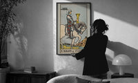 Knight of Cups print in a slim black frame being hung on a sunlit wall in a monochrome room