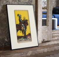 Knight on horse holding pentacle print in a black frame leaning beside a vintage door on parquet
