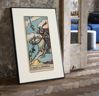 Armored knight riding horse with sword print in a black frame leaning beside a vintage door on parquet