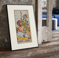 Knight riding horse holding wand print in a black frame leaning beside a vintage door on parquet