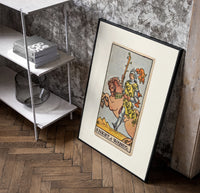 Knight riding horse holding wand poster in a black frame leaning beside a shelf in a raw-plaster loft