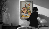 Knight of Wands print in a slim black frame being hung on a sunlit wall in a monochrome room