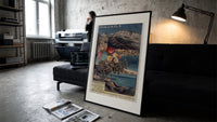 French Riviera coastal railway scene print in a slim black frame leaning on a dark sofa in a concrete print studio