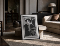 Man in hat and scarf print in a black frame leaning on a travertine table in a sunlit lounge