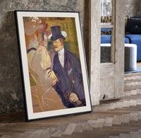 Man in top hat with women print in a black frame leaning beside a vintage door on parquet