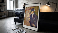 Man in top hat with women print in a slim black frame leaning on a dark sofa in a concrete print studio